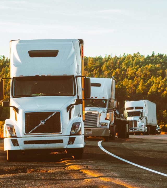 Three semi trucks driving on a highway through a forested landscape in Arizona.