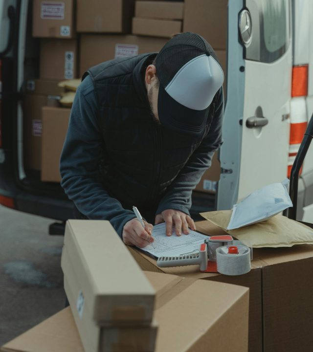 Courier organizing packages from a van, preparing for delivery in a logistics setting.